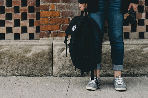 Student standing by brick wall holding backpack